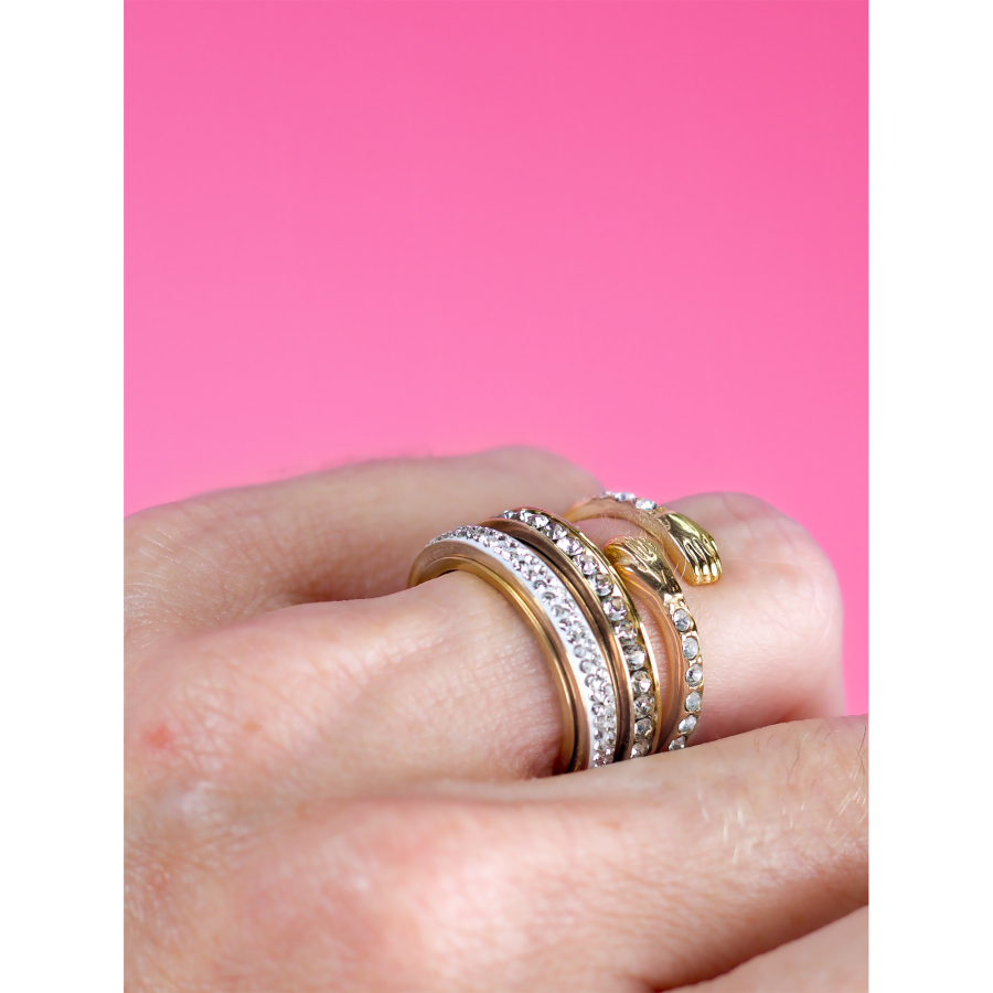 Forgyldte stacking-ringe med zirkoner på hånd – elegant og moderne look fra LÉ MOSCH mod pink baggrund